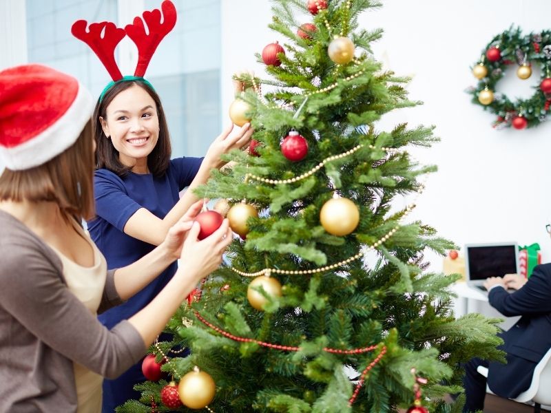 Woman in reindeer antlers decorating office xmas tree