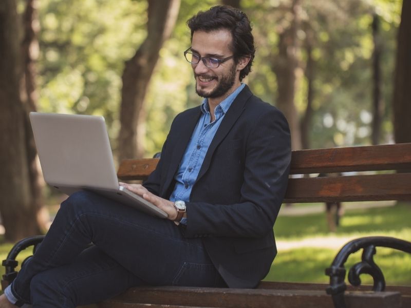 A picture of a man sitting on a bench and working on a laptop